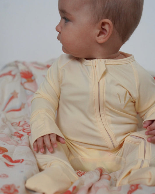Baby in a yellow outfit sitting on a floral blanket