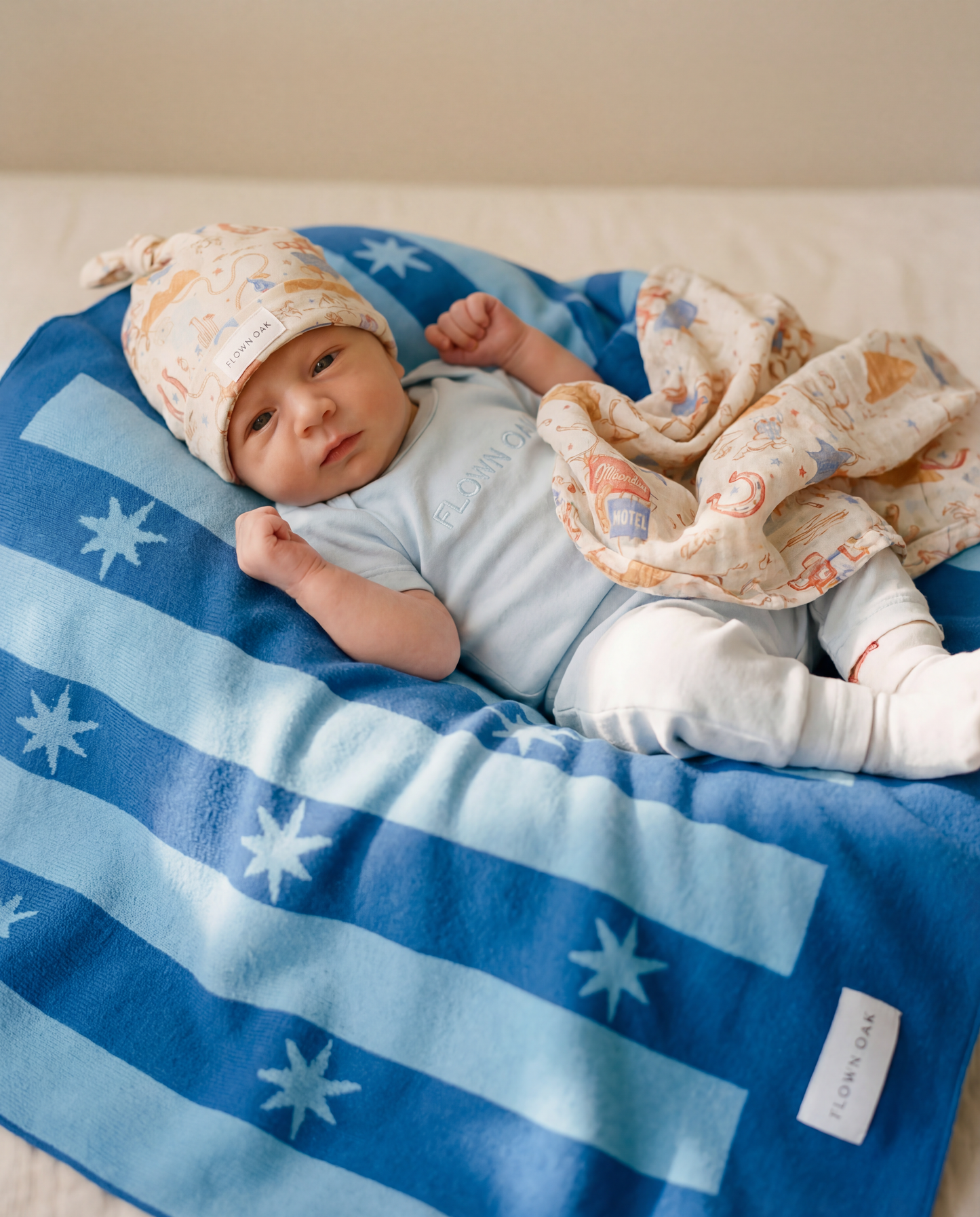 Newborn baby lying on a blue blanket with star patterns, wearing a light blue outfit and white hat.