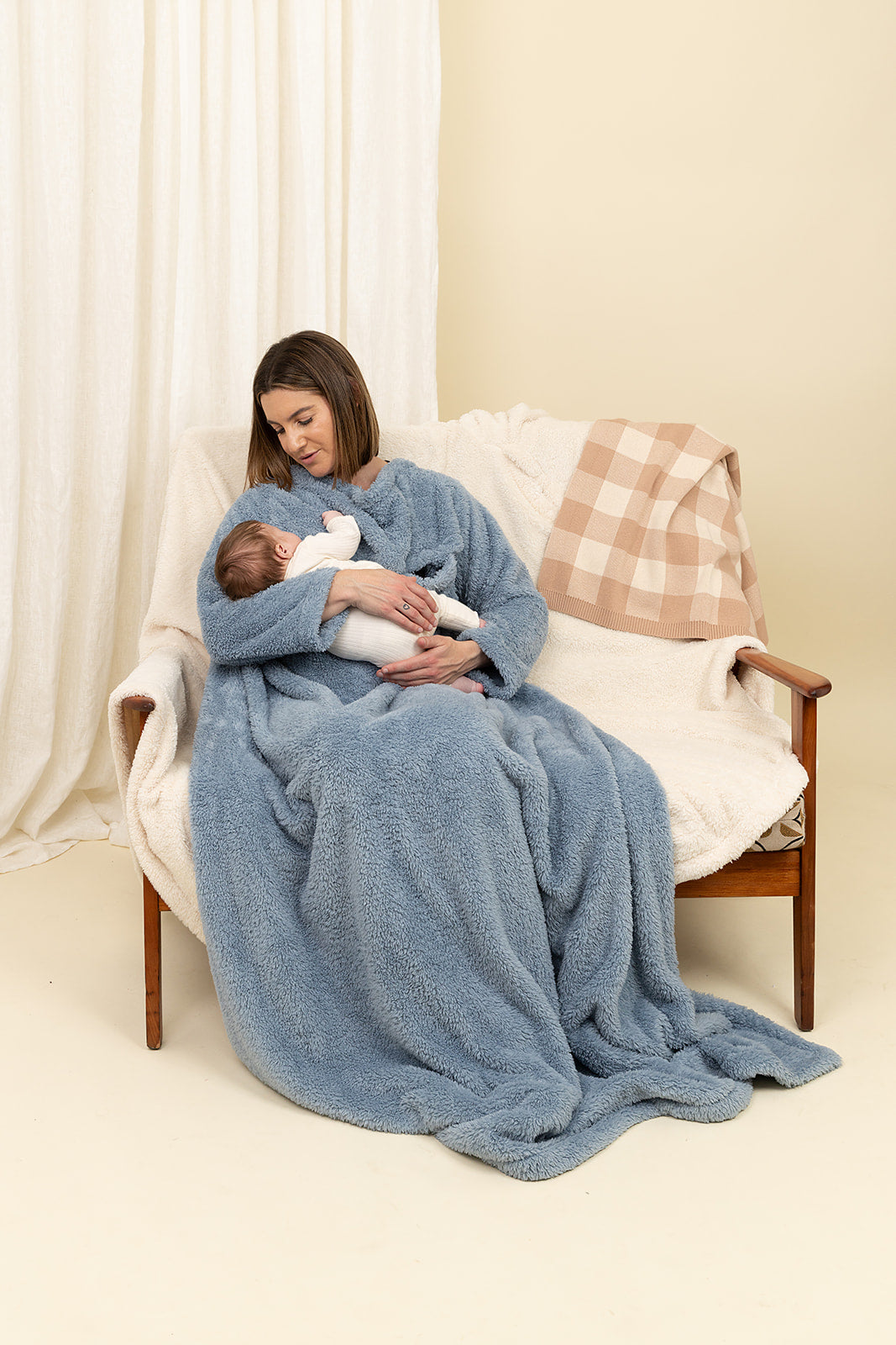 Woman holding a baby wrapped in a blue blanket on a white couch.