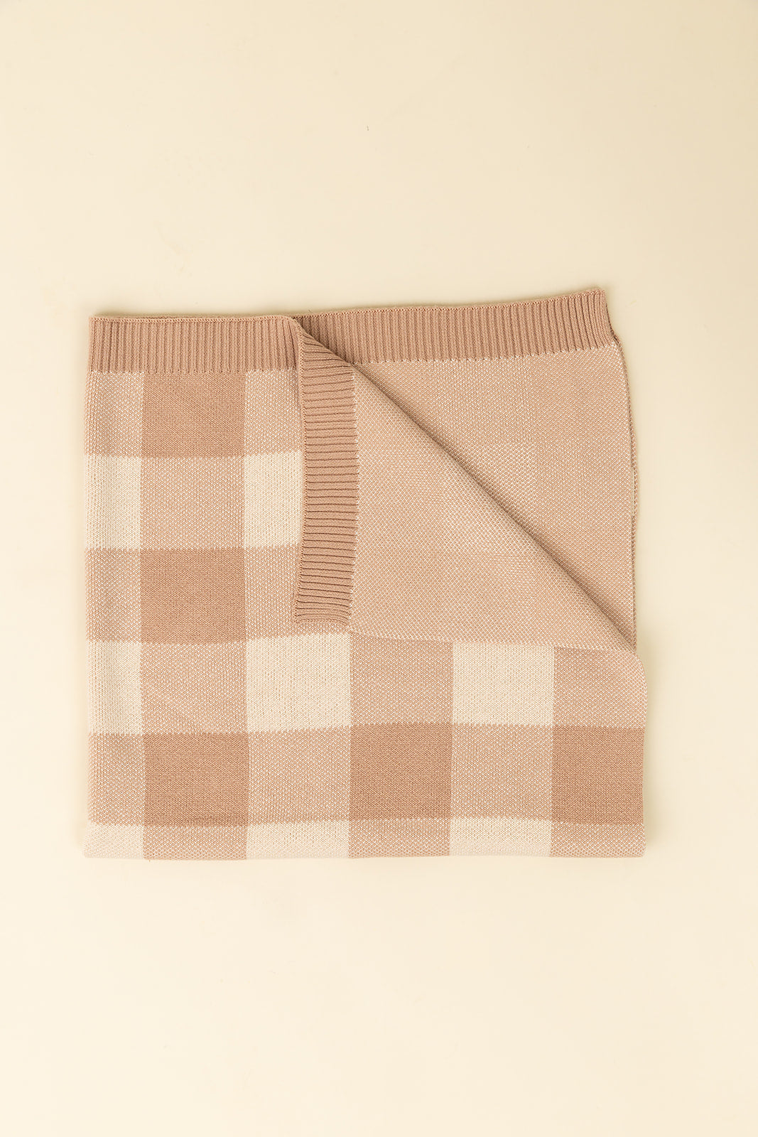 Folded checkered blanket with brown and beige pattern on a beige background