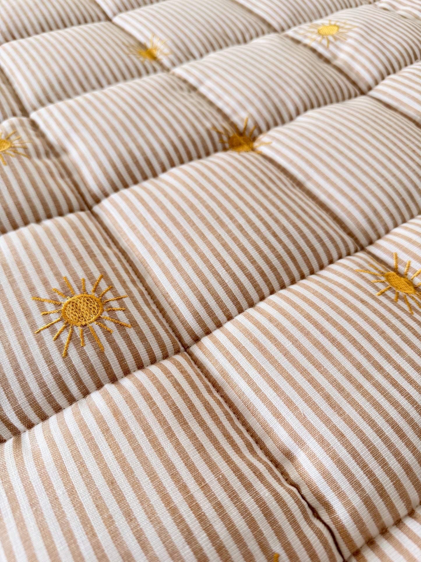 Close-up of a quilt with sun patterns on a beige and white striped background