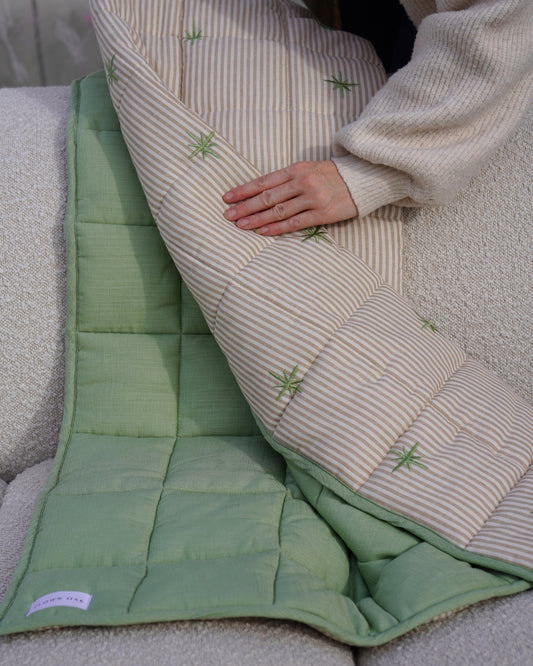 A green and beige quilt draped on a couch