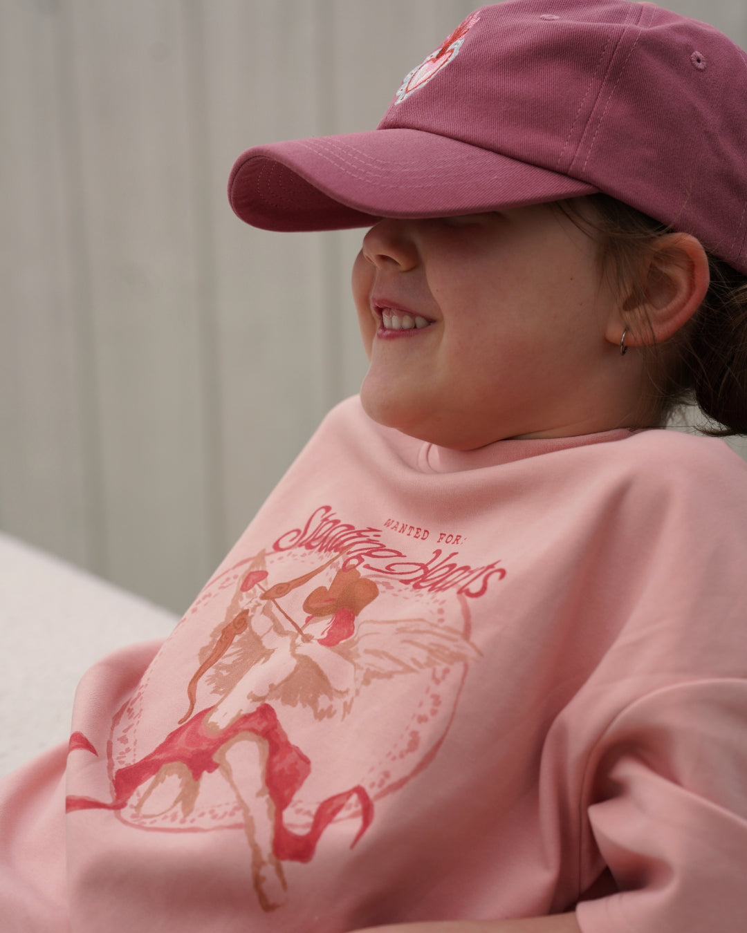 Person wearing a pink sweatshirt with a graphic design and a matching pink cap.