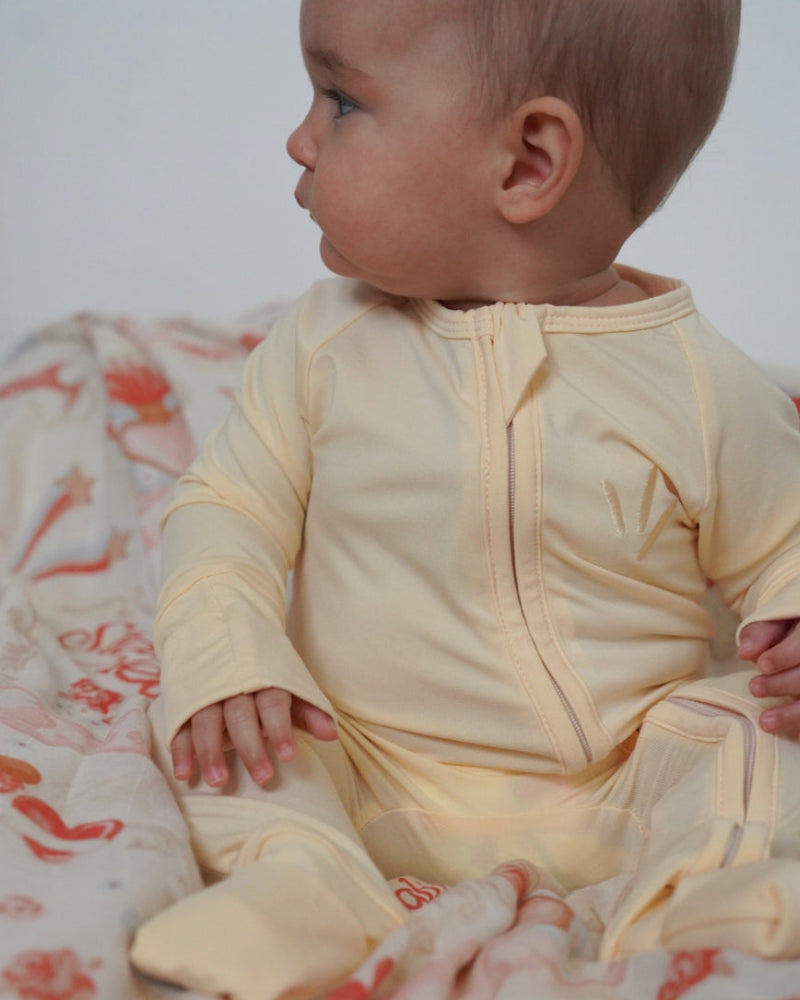 Baby in a yellow outfit sitting on a floral blanket