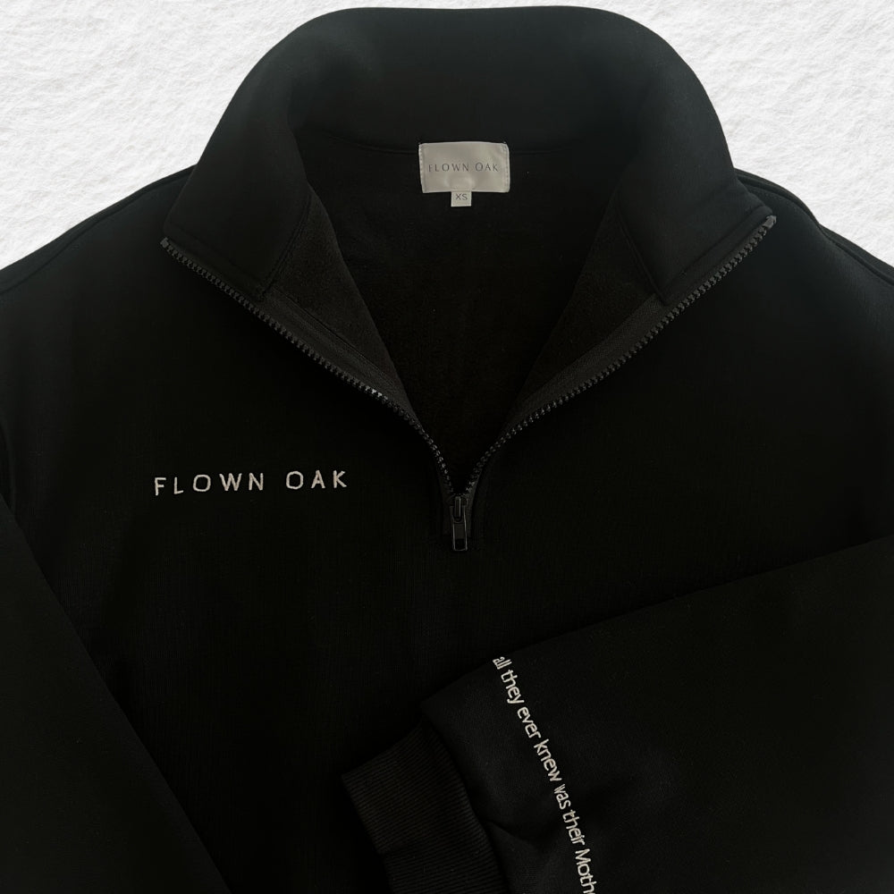 Black jumper with 'Flown Oak' branding on a textured gray background