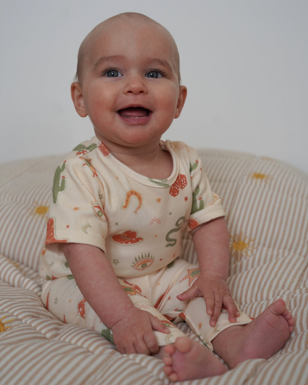 Baby sitting on a striped surface wearing a patterned outfit.