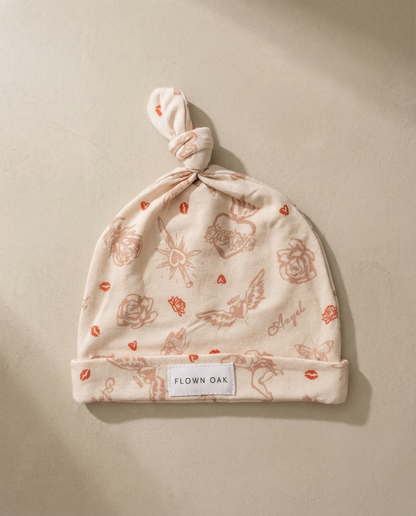 Baby hat with floral pattern and 'Flown Oak' label on a beige background