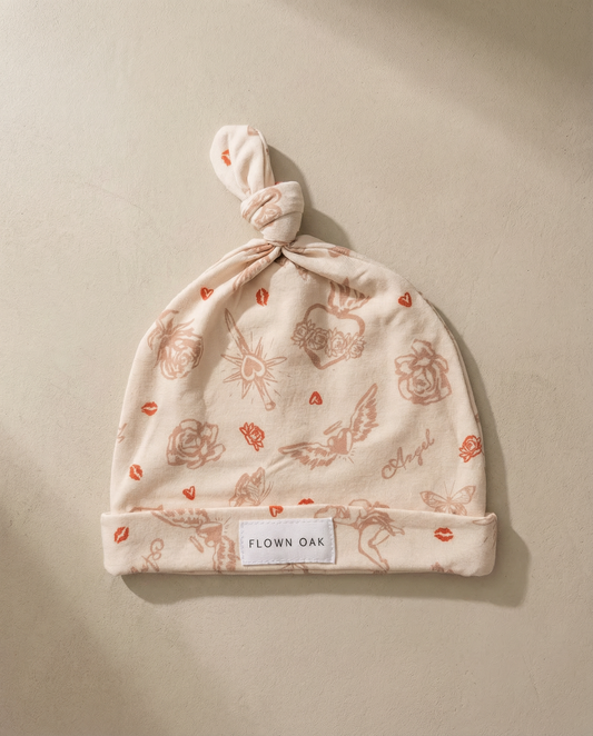 Baby hat with floral pattern and 'Flown Oak' label on a beige background