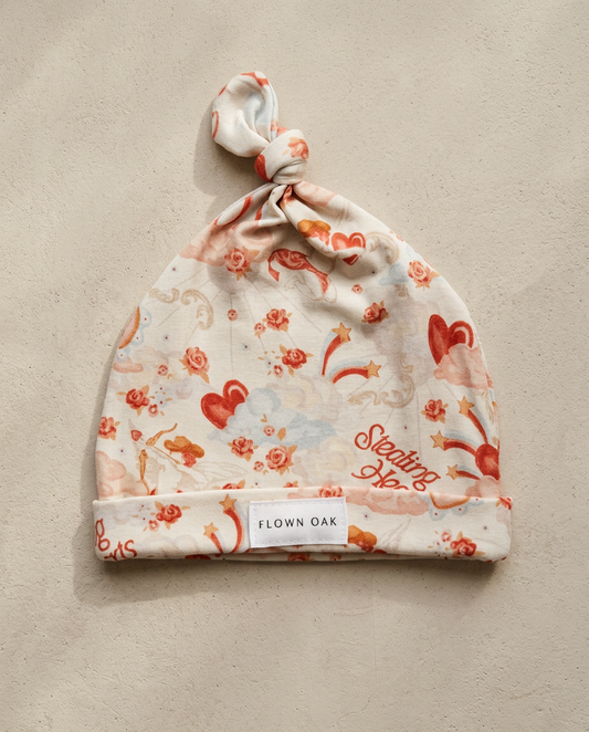 Floral patterned baby hat with 'Flown Oak' label on a beige background