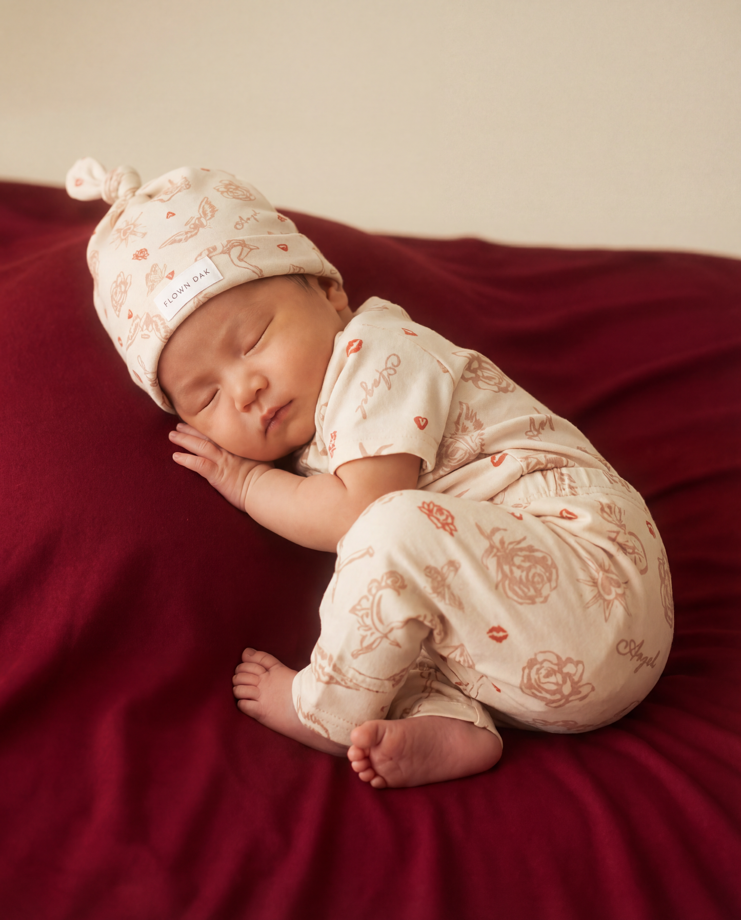 Newborn baby sleeping on a red blanket wearing a matching outfit and hat.