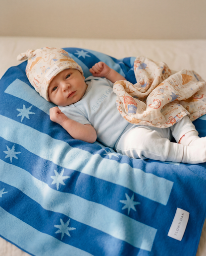 Newborn baby lying on a blue blanket with star patterns, wearing a light blue outfit and white hat.