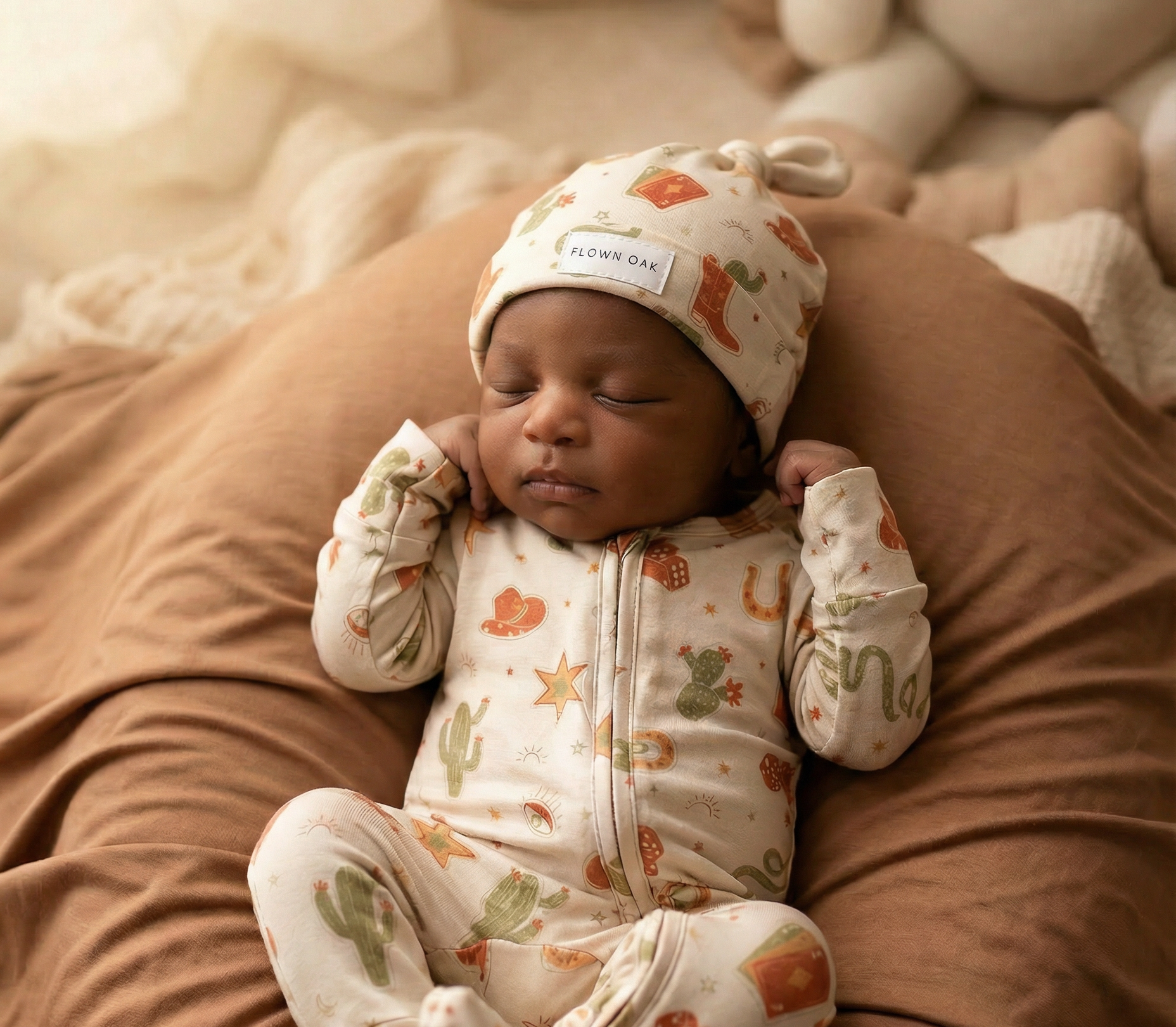 Newborn baby in a patterned outfit and hat lying on a brown surface
