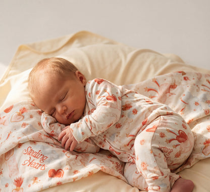 Baby sleeping on a bed with a patterned blanket and pajama set.