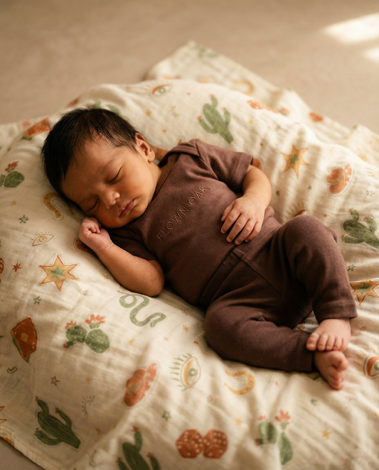 Newborn baby in a brown outfit lying on a patterned blanket