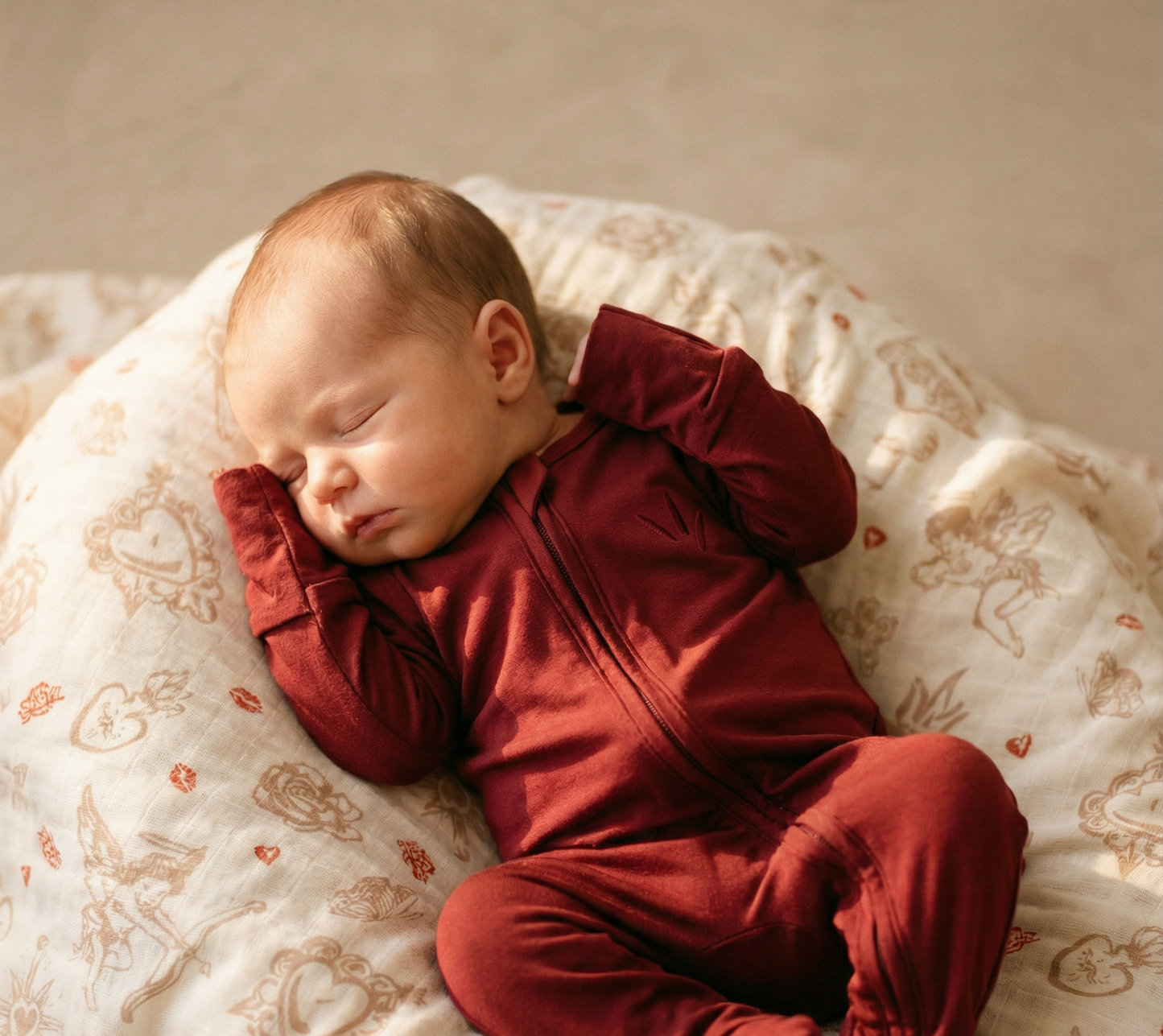 Newborn baby in a red outfit sleeping on a patterned blanket