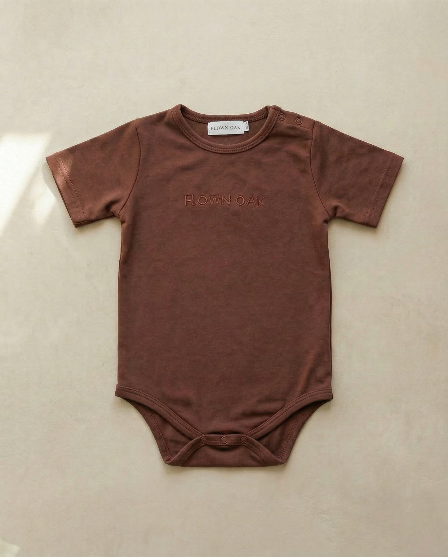 Brown baby onesie with 'Happy' printed on it, on a beige background