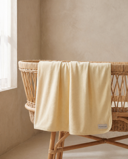 Yellow swaddle draped over a wicker bassinet in a softly lit room.