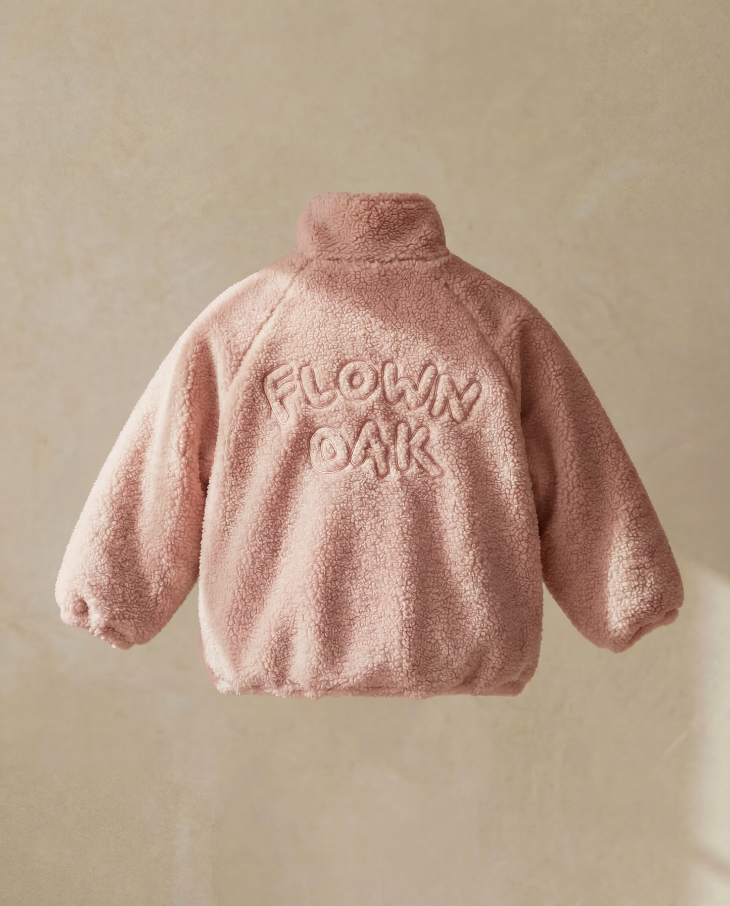 Pink fluffy jacket with 'FLOWN OAK' text on a beige background