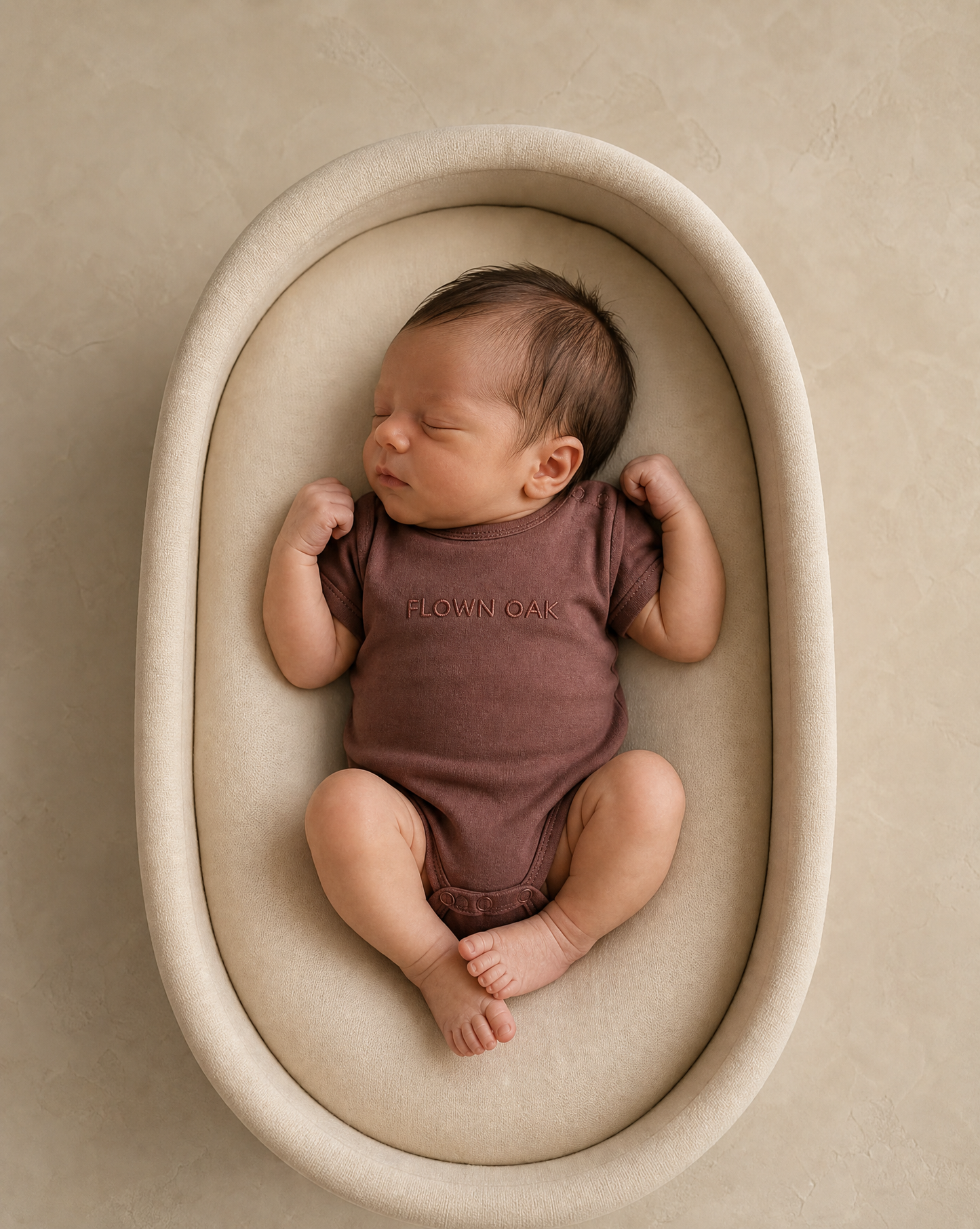 Newborn baby in a brown onesie lying in a beige crib.