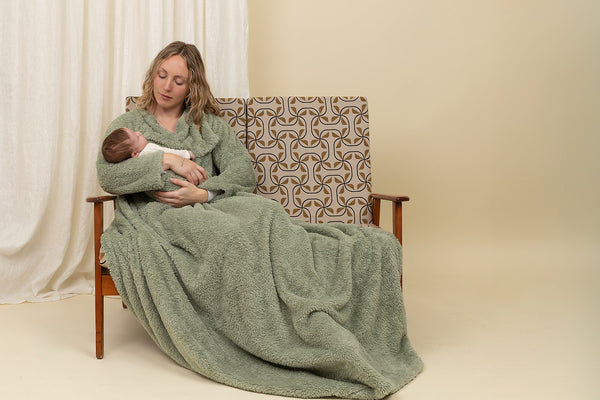 Woman holding a baby wrapped in a green blanket sitting on a patterned chair.