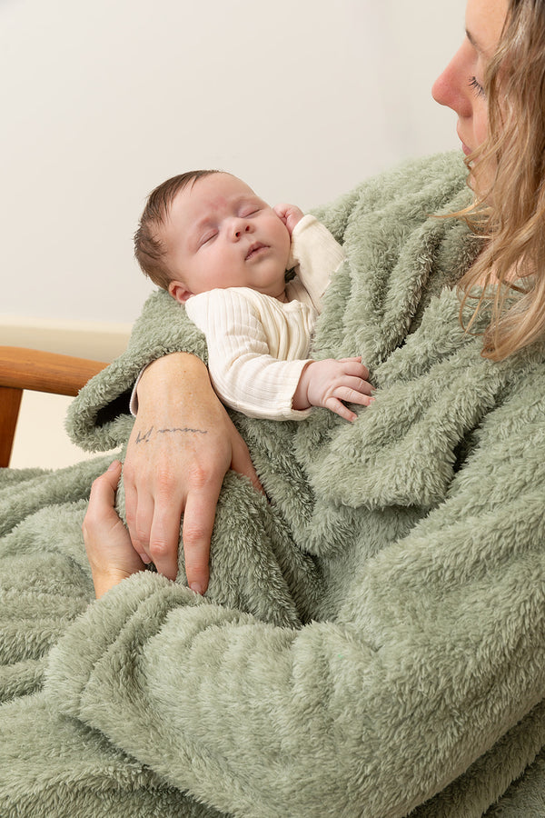 Baby wrapped in a green blanket being held by a person against a neutral background