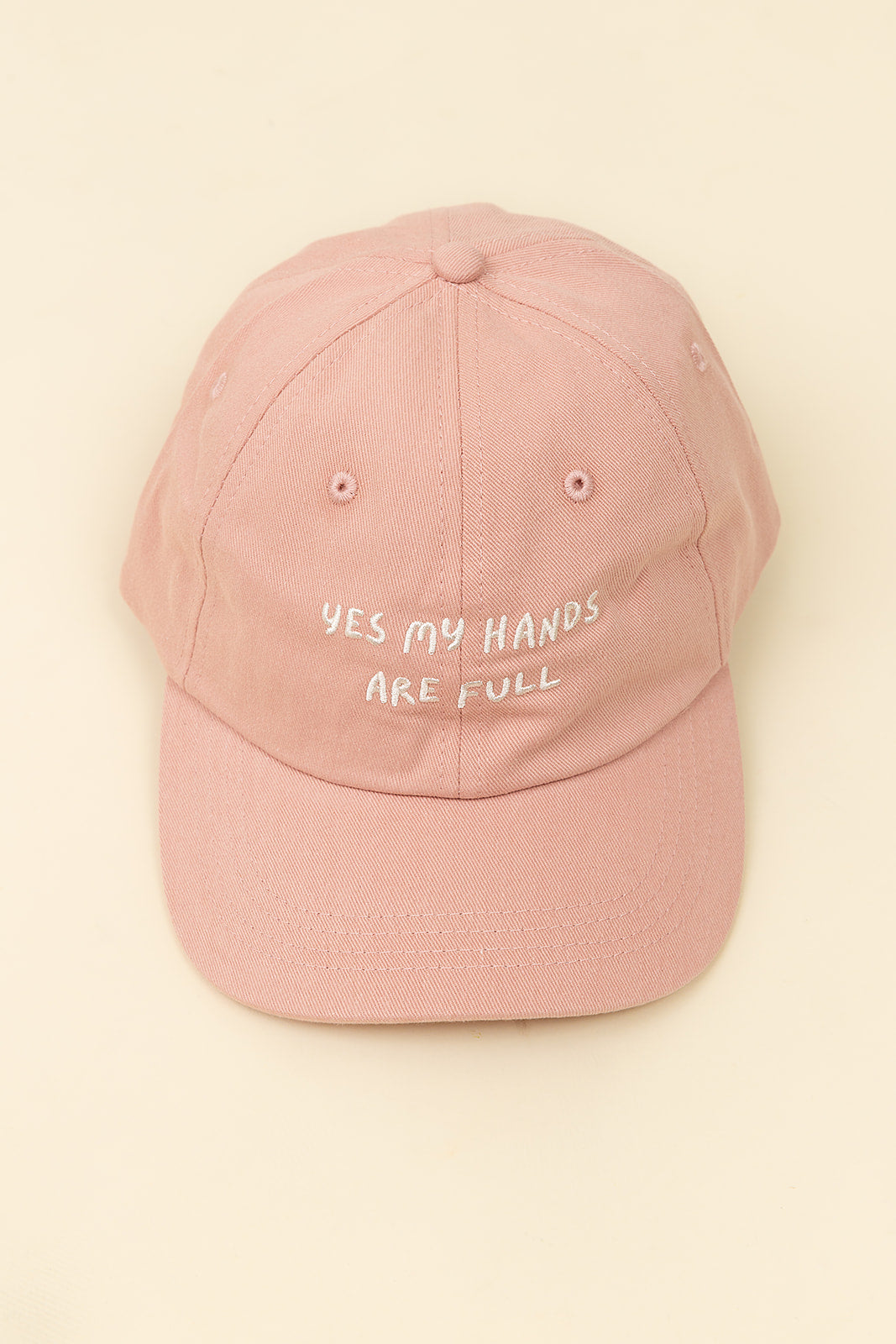 Pink cap with 'YES MY HANDS ARE FULL' text on a beige background
