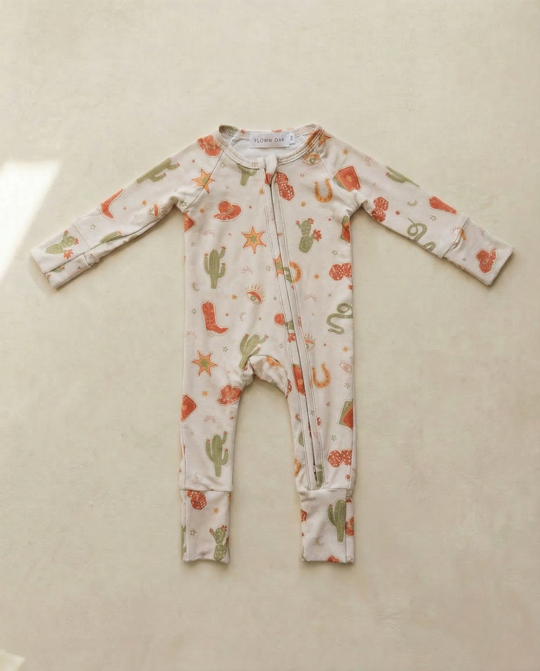 Baby onesie with cactus and flower pattern on a beige surface