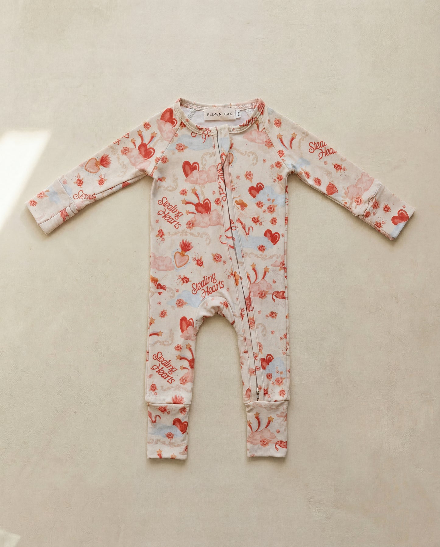 Baby onesie with heart and cherry pattern on a beige surface