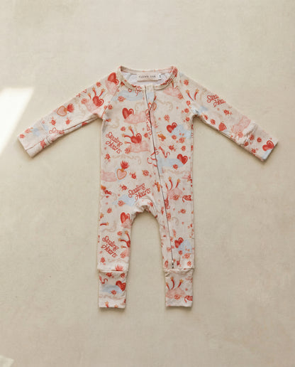 Baby onesie with heart and cherry pattern on a beige surface