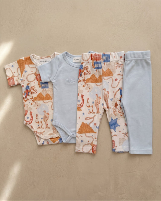 Baby clothing set with onesie, shirt, and pants on a beige background