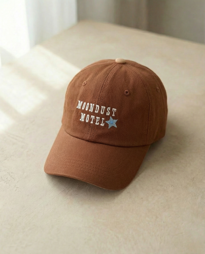 Brown cap with 'Moondust Motel' text on a beige surface