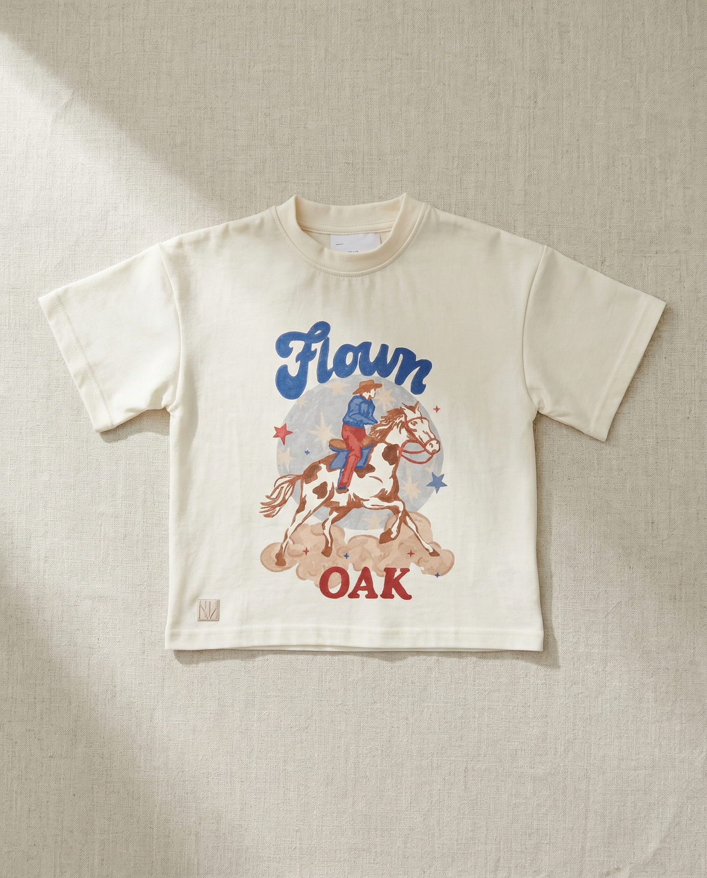 Children's t-shirt with a graphic of a person on a horse and text 'Flown Oak' on a textured beige background