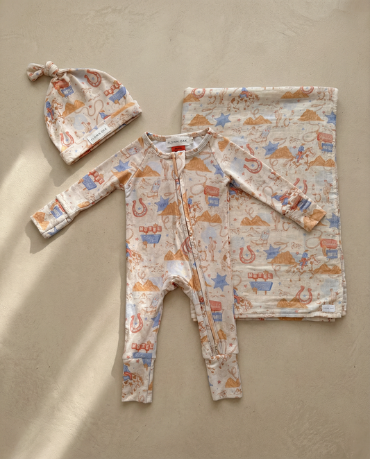 Baby outfit set with onesie, hat, and blanket featuring vehicle pattern on a beige background