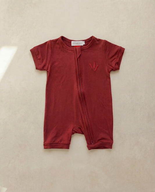 Red baby romper with a small logo on a beige background