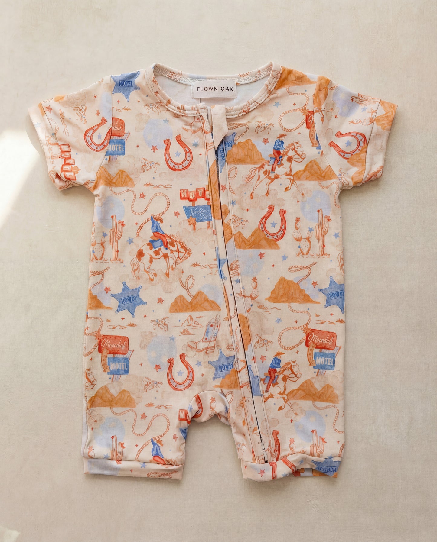 Baby romper with cowboy pattern on a beige surface