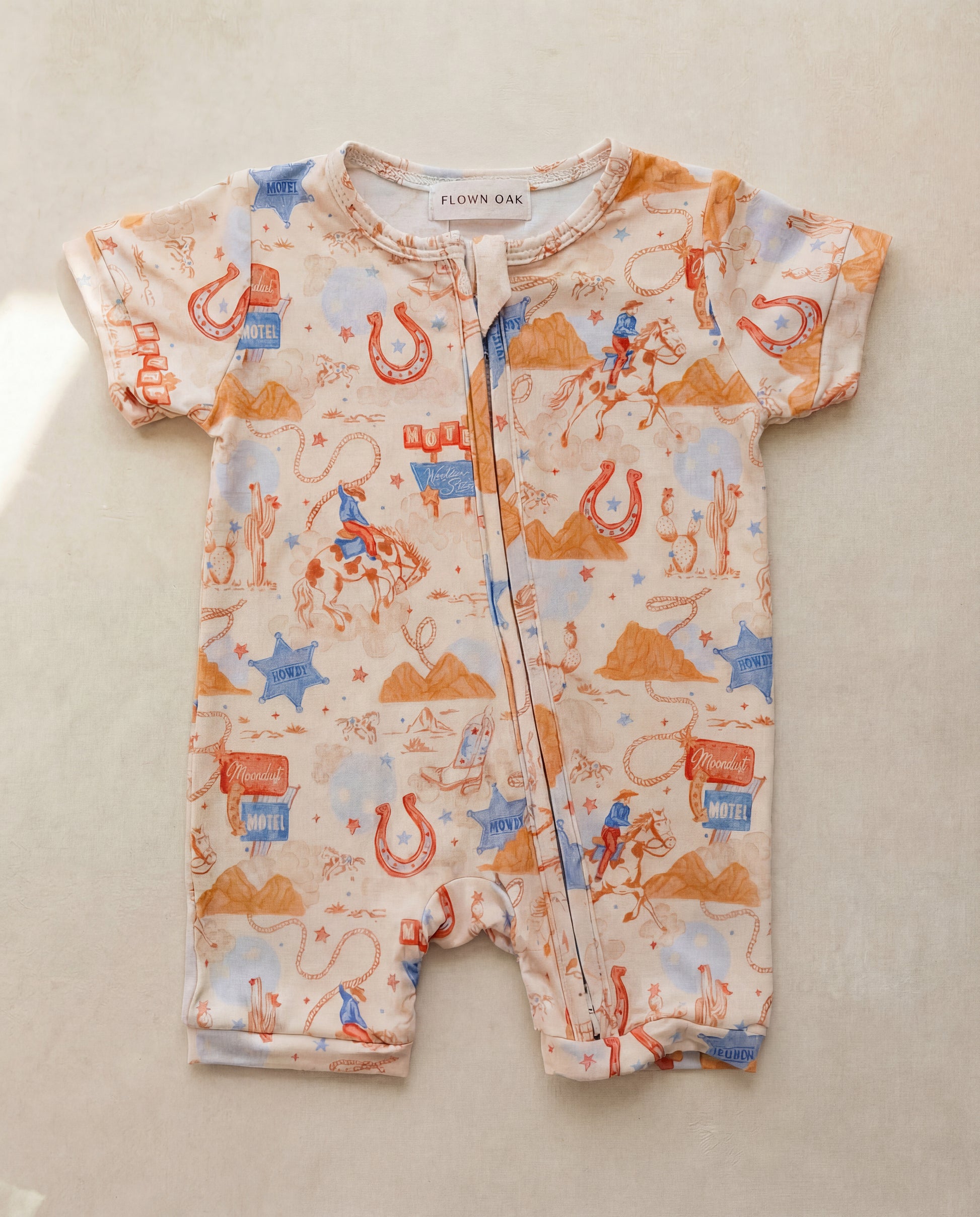 Baby romper with cowboy pattern on a beige surface
