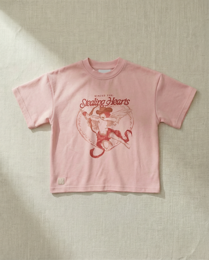 Pink t-shirt with red graphic and text on a textured beige background