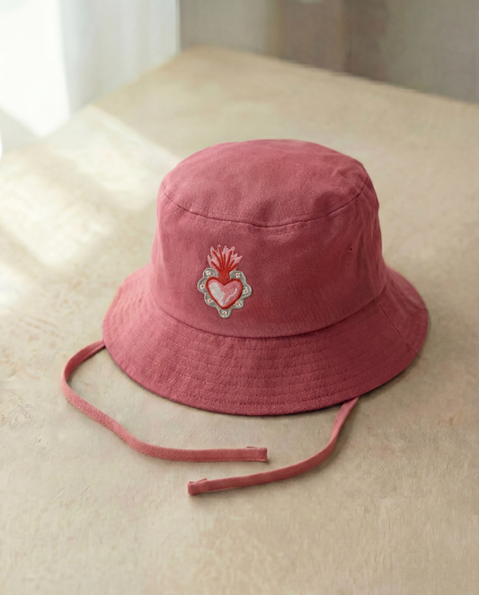 Pink bucket hat with a heart design on a beige surface