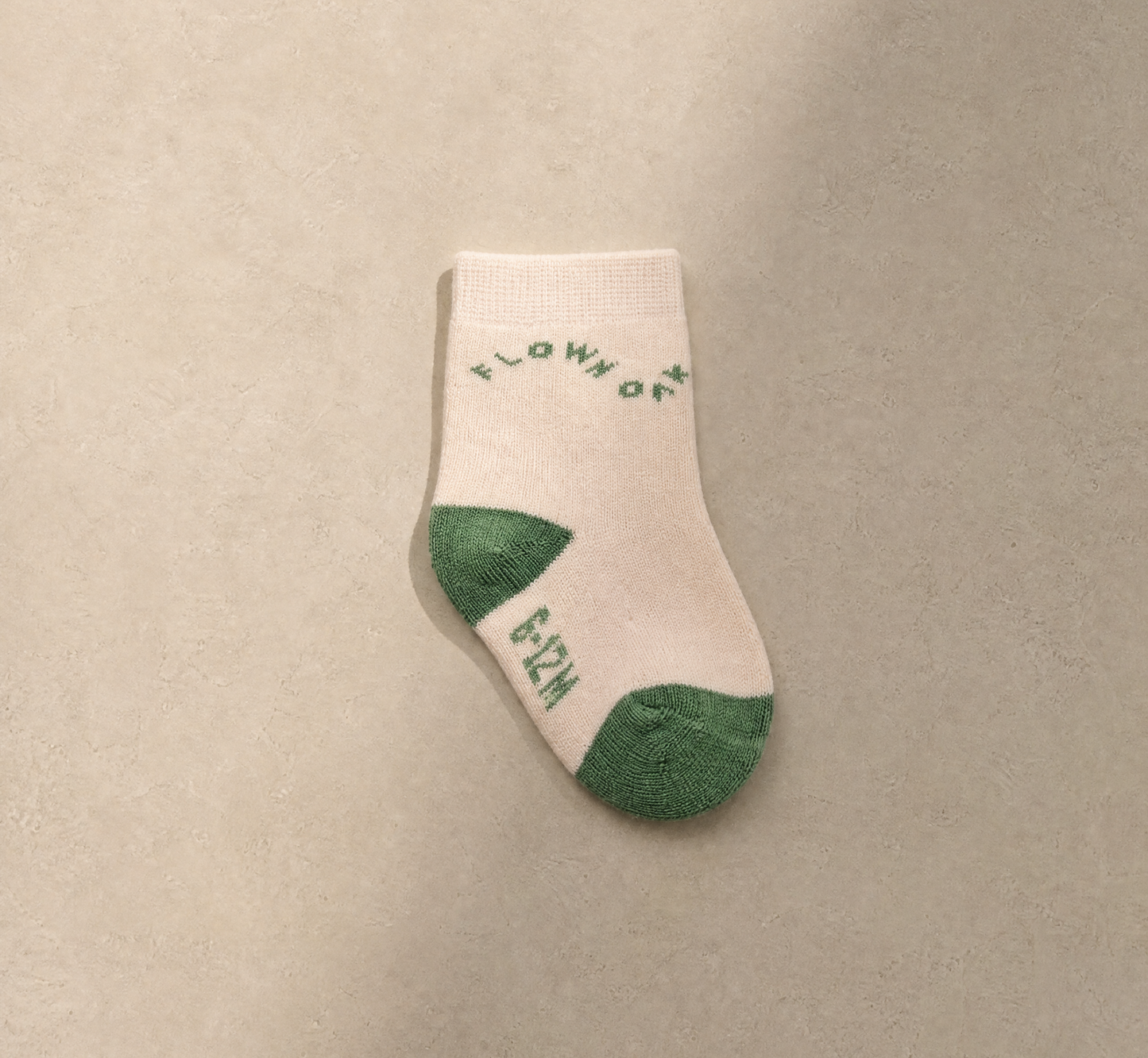 A single off-white knit sock with green heel and toe accents, featuring the words 'FLOW OF LIFE' in green on the side, displayed on a neutral beige textured background.