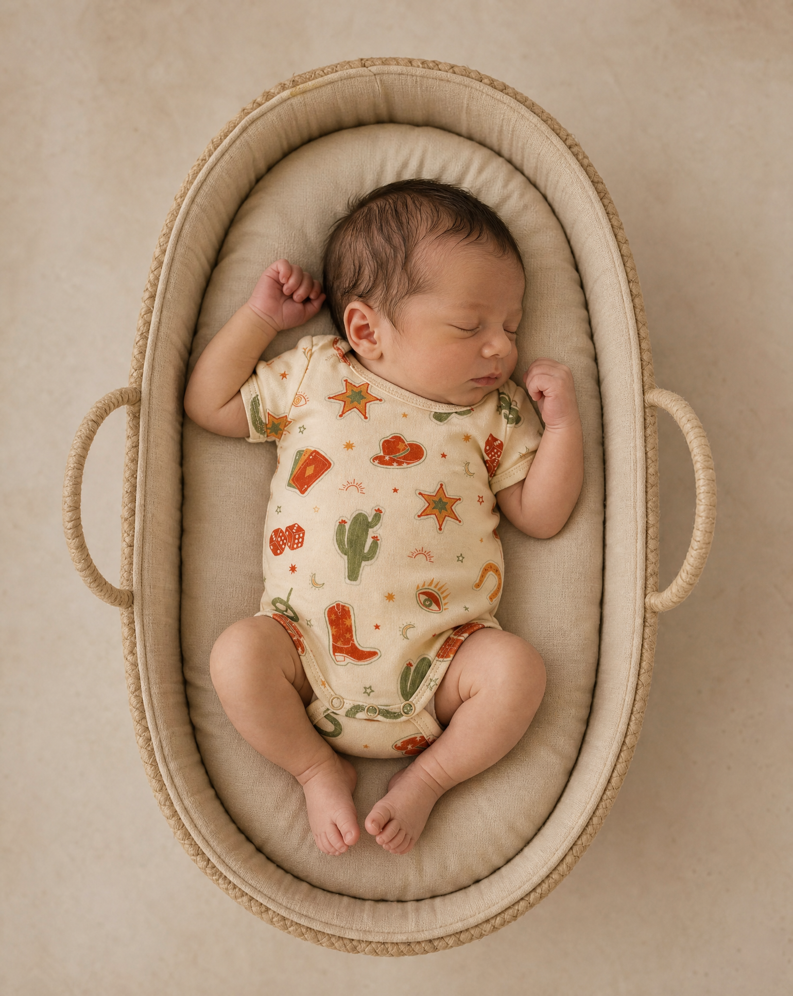 Newborn baby sleeping in a Moses basket with a patterned outfit.