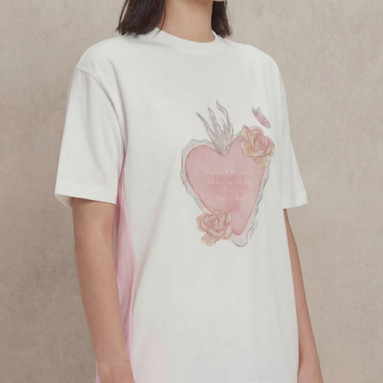 A video of a woman wearing a white tshirt with a heart image printed on the front